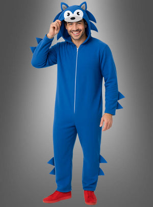 Eine Person, die den „Blauer Videogame Igel Overall für Erwachsene“ trägt – aus blauem Stoff, mit Stacheln und einer Kapuze mit Cartoon-Gesicht, das an Sonic the Hedgehog erinnert –, lächelt vor einem grauen Hintergrund. Damit ist er das ideale Erwachsenenkostüm für Fans, die nach einer Verkleidung als legendären Videospielhelden suchen.