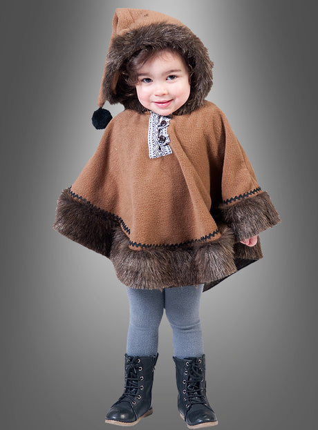 Ein Kleinkind trägt den „Eskimo Nalu Umhang für Kinder“, einen braunen Umhang mit Kapuze und Pelzbesatz, dazu graue Leggings und schwarze Stiefel, und steht vor einem grauen Hintergrund mit Farbverlauf.