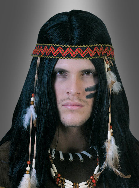 Eine Person in einem Indianerkostüm, die eine Indianerperücke mit Stirnband trägt – bestehend aus einer langen schwarzen Perücke und einem rot gemusterten Stirnband mit Federn –, sowie Gesichtsbemalung, Perlenschmuck und weitere Federn, posiert vor einem grauen Hintergrund.