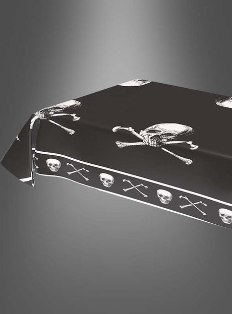 Eine Piraten-Tischdecke (270 × 136 cm) mit Totenkopf-Motiv in Schwarz und weißen Totenköpfen bedeckt einen rechteckigen Tisch vor einem grauen Farbverlaufshintergrund – perfekt für jeden abenteuerlichen Kindergeburtstag.