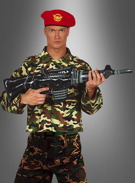 Ein Mann in einer Tarnuniform und einem roten Barett hält das „Aufblasbare Maschinengewehr 90 cm“, eine große, aufblasbare Waffe im Science-Fiction-Stil – perfekt für Ihr nächstes Karnevalskostüm –, während er vor einem schlichten grauen Hintergrund steht.