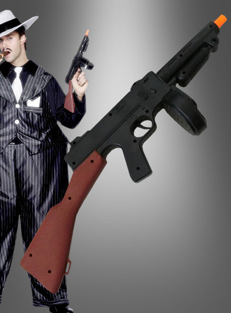 Eine Person in einem Nadelstreifenanzug und mit Hut erinnert an den klassischen Mafia-Stil von Al Capone und hält die „Mafia Tommy Gun Gewehr schwarz“ in der Hand – eine spielerische Anspielung auf eine Mottoparty im Stil der „Roaring Twenties“. Im Vordergrund ist eine Nahaufnahme der „Mafia Tommy Gun Gewehr schwarz“ mit ihrer markanten orangefarbenen Mündungsspitze zu sehen, die der Gangster-Party einen authentischen Touch verleiht.