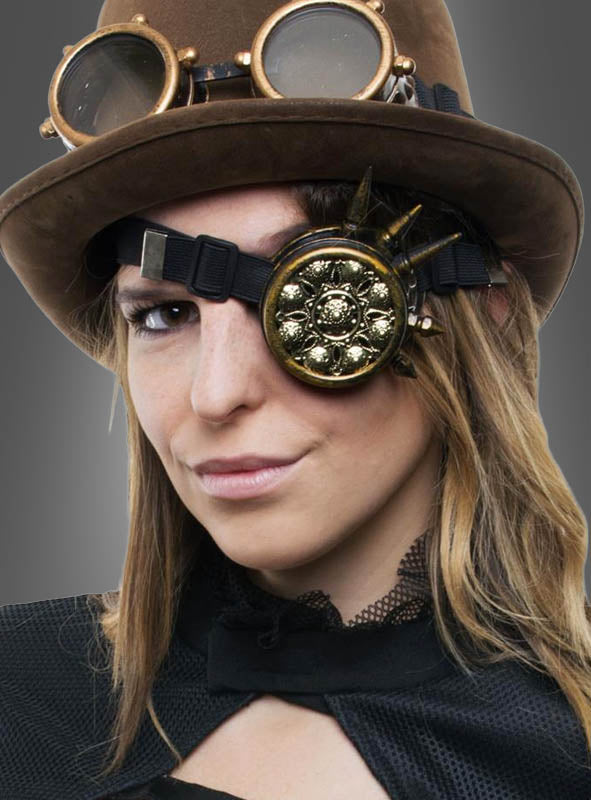 Eine schwarz gekleidete Person trägt einen braunen Steampunk-Hut mit Schutzbrille und einem verzierten goldenen Okular, elegant ergänzt durch das „Steampunk Monokel Unisex“ als stilvolles Steampunk-Accessoire, vor einem grauen Hintergrund mit Farbverlauf.