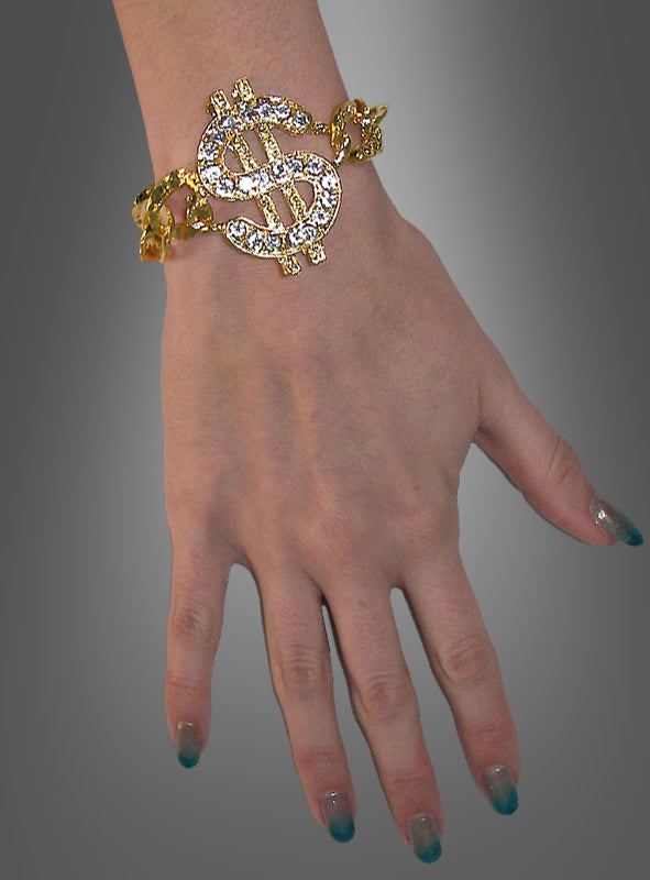 Eine Hand, die das „Pimp Armband mit Dollarzeichen“ trägt, mit einem großen, mit Edelsteinen besetzten Dollarzeichen-Anhänger, vor einem grauen Hintergrund mit Farbverlauf.