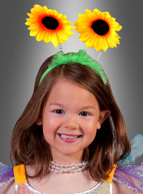 Ein junges Mädchen lächelt und trägt den „Haarreif mit Sonnenblumen“ – mit zwei großen künstlichen Sonnenblumen an Federn – als Haaraccessoire sowie eine Perlenkette vor einem grauen Hintergrund mit Farbverlauf.