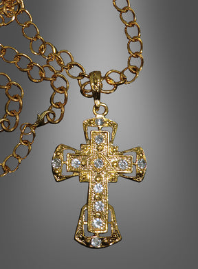 Deluxe-Kreuz-Medaillon mit Kette – ein elegantes Accessoire für festliche Anlässe, inspiriert von der Tradition eines katholischen Geistlichen, präsentiert als goldene Halskette mit aufwendig verziertem Kreuzanhänger und mehreren kleinen, klaren Schmucksteinen vor einem grauen Farbverlaufshintergrund.