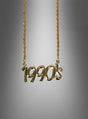Die goldfarbene Halskette im Stil der 1990er Jahre besticht durch einen Anhänger mit der Aufschrift „1990s“ vor einem dezent grau verlaufenden Hintergrund – das ideale Accessoire für dein Hip-Hop-Kostüm oder als trendige Kette im Stil der 90er Jahre.