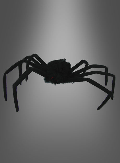 Eine schwarze, flauschige „Schwarze Spinne“ (50 cm) mit langen Beinen und kleinen roten Augen hebt sich deutlich von einem grauen Hintergrund mit Farbverlauf ab – diese Riesenspinne ist die perfekte Halloween-Dekoration, um Ihrem Raum eine gruselige Note zu verleihen.