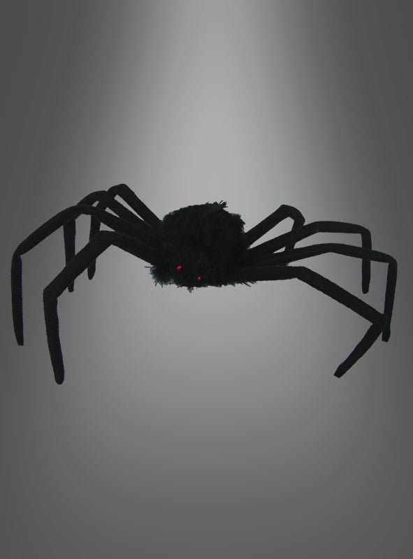 Eine schwarze, flauschige „Schwarze Spinne“ (50 cm) mit langen Beinen und kleinen roten Augen hebt sich deutlich von einem grauen Hintergrund mit Farbverlauf ab – diese Riesenspinne ist die perfekte Halloween-Dekoration, um Ihrem Raum eine gruselige Note zu verleihen.