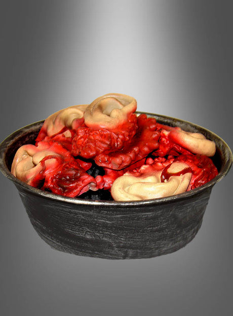Eine schwarze Schüssel mit abgeschnittenen Ohren – perfekt für Ihre Halloween-Dekoration – enthält mehrere rote, strukturierte Objekte mit ohrähnlichen Formen, die auf einem grau verlaufenden Hintergrund liegen.
