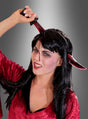 Eine Frau in einem roten Samtop, die das „Deluxe blutendes Messer im Kopf“-Attrappen-Stirnband trägt – komplett mit Kunstblut auf der Stirn – posiert vor einem grauen Hintergrund mit Farbverlauf: das perfekte Halloween-Kostüm-Accessoire für einen gruseligen Look.