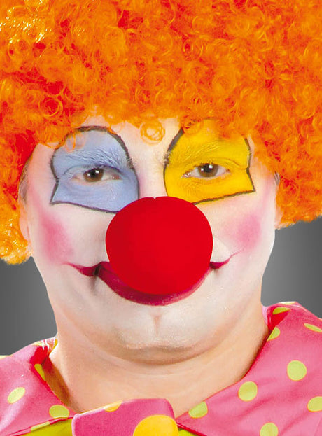 Eine als Clown verkleidete Person mit einer orangefarbenen Lockenperücke, einer roten Nase, bunter Gesichtsbemalung und einem Kostüm aus rosa Stoff mit gelben Punkten – abgerundet durch eine leuchtende „Clownnase 7 cm Rot Jumbo“ für den ganz besonderen verspielten Touch.