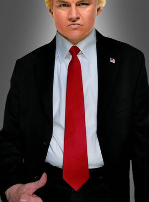 Eine Person in einem schwarzen Anzug, einem weißen Hemd und dem „Rote Krawatte für Trump“-Kostüm mit einer Anstecknadel in Form der amerikanischen Flagge, die vor einem grauen Hintergrund steht – ideal als Trump-Parodie-Kostüm.