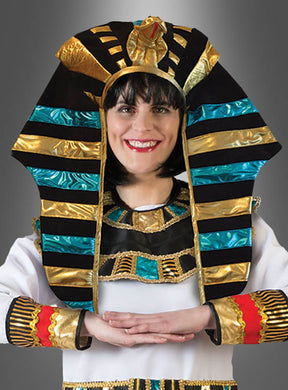 Eine Person, die den „Pharao Kopfschmuck gold-blau“ trägt – mit auffälligen blauen und goldenen Streifen und bunten Verzierungen –, lächelt mit verschränkten Armen.