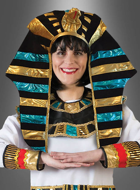 Eine Person, die den „Pharao Kopfschmuck gold-blau“ trägt – mit auffälligen blauen und goldenen Streifen und bunten Verzierungen –, lächelt mit verschränkten Armen.