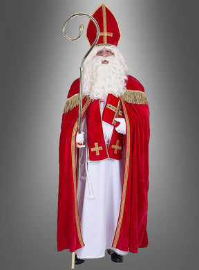 Eine als Heiliger Nikolaus verkleidete Person, die ein rotes Gewand mit goldenen Verzierungen trägt, einen Stab und ein Buch in den Händen hält und vor einem grauen Hintergrund steht – die perfekte Inspiration, wenn Sie ein günstiges XL-XXL-Kostüm des Heiligen Bischofs Nikolaus kaufen möchten oder auf der Suche nach dem idealen Nikolauskostüm für die bevorstehenden Festlichkeiten sind.