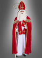 Eine als Heiliger Nikolaus verkleidete Person, die ein rotes Gewand mit goldenen Verzierungen trägt, einen Stab und ein Buch in den Händen hält und vor einem grauen Hintergrund steht – die perfekte Inspiration, wenn Sie ein günstiges XL-XXL-Kostüm des Heiligen Bischofs Nikolaus kaufen möchten oder auf der Suche nach dem idealen Nikolauskostüm für die bevorstehenden Festlichkeiten sind.
