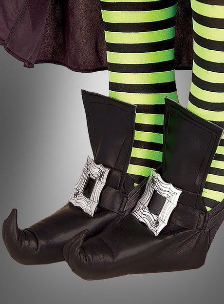 Eine Person trägt Hexenschuhüberzieher im Hexenschuh-Look mit Spinnennetz-Schnallen sowie grün-schwarz gestreifte Strumpfhosen und steht vor einem grauen Hintergrund.