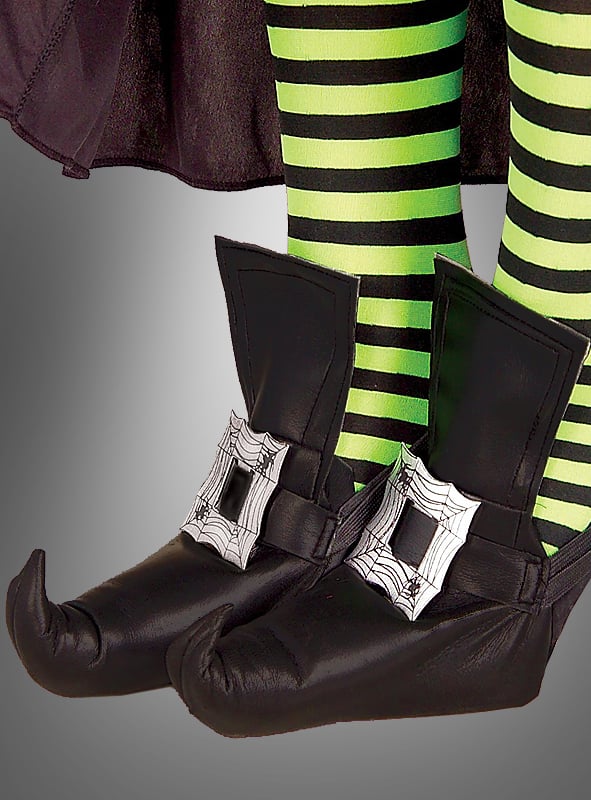Eine Person trägt Hexenschuhüberzieher im Hexenschuh-Look mit Spinnennetz-Schnallen sowie grün-schwarz gestreifte Strumpfhosen und steht vor einem grauen Hintergrund.