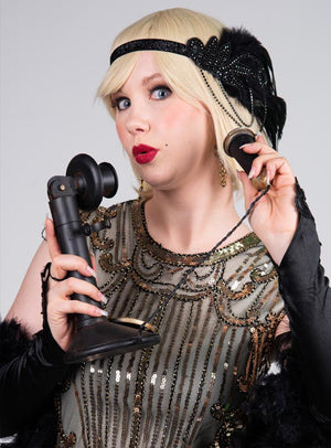 Eine Frau in der Kleidung einer Flapper aus den 1920er Jahren hält den Kerzenständer „Retro Telefon 20er Jahre Deko“ in der Hand und blickt überrascht – ein perfektes Herzstück für jede Dekoration im Stil der 20er Jahre oder ein retro-inspiriertes Ambiente.