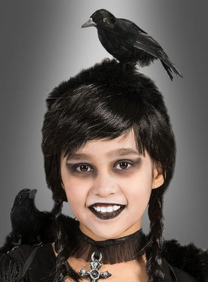 Ein Kind mit schwarzen Zöpfen, dunklem Augen-Make-up und schwarzem Lippenstift trägt ein Halsband mit einem Kreuz sowie auffällige Gothic-Accessoires. Sie wird von zwei schwarzen Raben begleitet – einer sitzt auf ihrem Kopf wie beim „Haarreif mit Rabe und Federn“, der andere auf ihrer Schulter –, vor einem grauen Hintergrund, wodurch sich dieser Look perfekt für jedes Halloween-Kostüm eignet.
