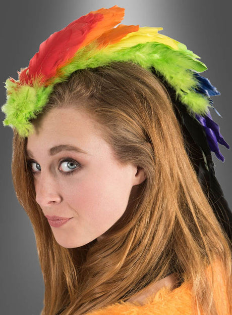 Eine Frau mit langen braunen Haaren trägt den „Bunter Kopfschmuck Paradiesvogel Papagei“ – ein farbenfrohes, regenbogenfarbenes Feder-Mohawk-Haaraccessoire, das sich perfekt für den Karneval eignet –, während sie mit ausdruckslosem Blick vor einem grauen Hintergrund mit Farbverlauf in die Kamera schaut.