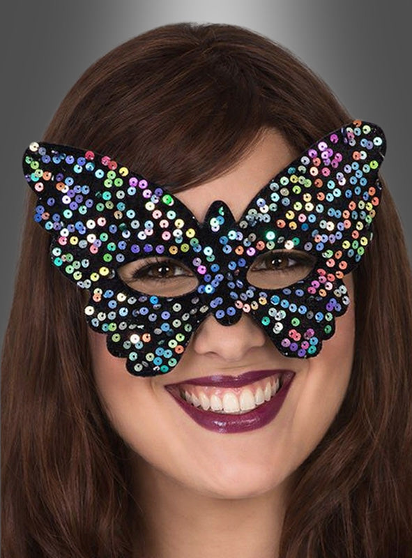 Eine Frau lächelt, während sie die „Schmetterling Augenmaske Pailletten“ trägt, ein farbenfrohes Karnevalsaccessoire, das mit bunten Pailletten verziert ist und sich vor einem grauen Hintergrund abhebt.