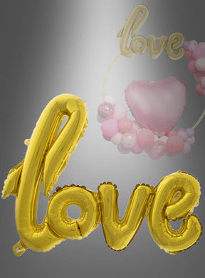 Goldfarbener Folienballon mit der Aufschrift „Love“ (100 cm), präsentiert vor einem festlichen Hintergrund, der durch einen rosa Herzballon und ein Arrangement aus rosa, weißen und goldenen Ballons ergänzt wird – eine ideale Hochzeitsdekoration mit dem eleganten goldenen „Love“-Folienballon (100 cm).