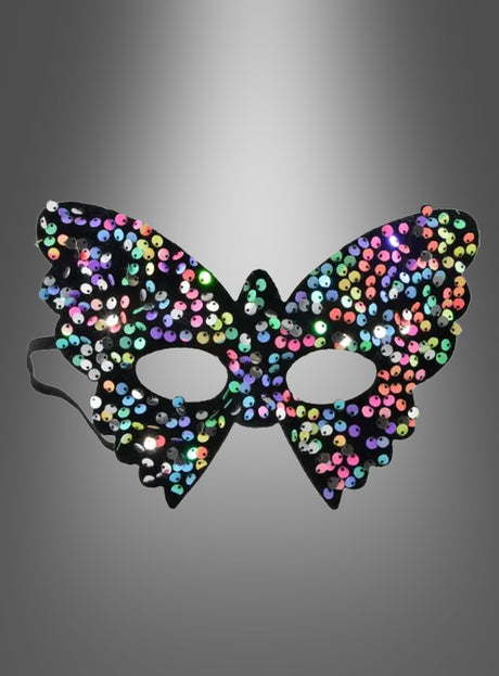 Vor einem grauen Hintergrund mit Farbverlauf ist eine schillernde Schmetterling-Augenmaske mit Pailletten zu sehen, die die Form eines Schmetterlings hat und mit bunten Pailletten verziert ist. Dieses farbenfrohe Accessoire ist die perfekte Wahl, um jede Karnevalsfeier zu einem unvergesslichen Erlebnis zu machen.