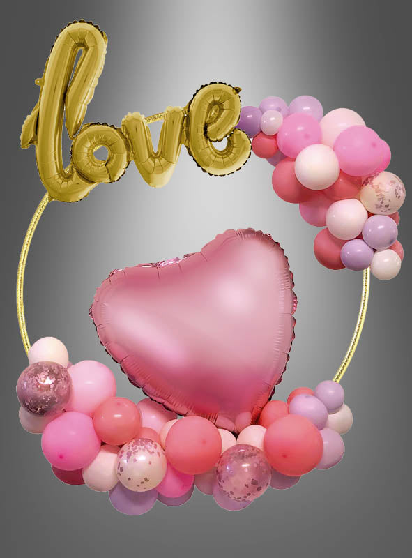 Der Ballonbogen 60 cm Deko-Ring in Gold besticht durch einen goldenen Liebesballon und einen rosa Herzballon, die wunderschön mit rosa, weißen und lila Ballons auf dem eleganten goldenen Ring arrangiert sind. Vor einem grauen Hintergrund mit Farbverlauf ist dieser schicke Ballonbogen-Deko-Ring perfekt, um jeder Feier eine stilvolle Partydekoration zu verleihen.