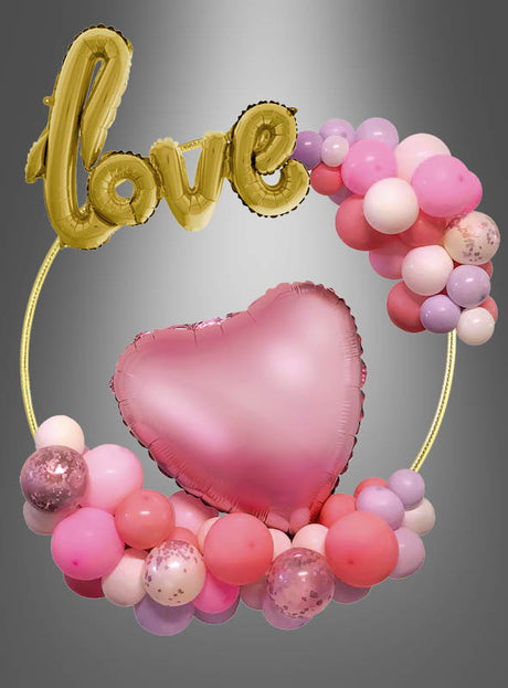 Der Ballonbogen 60 cm Deko-Ring in Gold besticht durch einen goldenen Liebesballon und einen rosa Herzballon, die wunderschön mit rosa, weißen und lila Ballons auf dem eleganten goldenen Ring arrangiert sind. Vor einem grauen Hintergrund mit Farbverlauf ist dieser schicke Ballonbogen-Deko-Ring perfekt, um jeder Feier eine stilvolle Partydekoration zu verleihen.