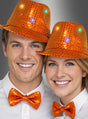 Zwei Personen, die leuchtend orangefarbene Trilby-Hüte mit LED und dazu passende orangefarbene Pailletten-Fliegen tragen und vor einem grauen Hintergrund in die Kamera lächeln.