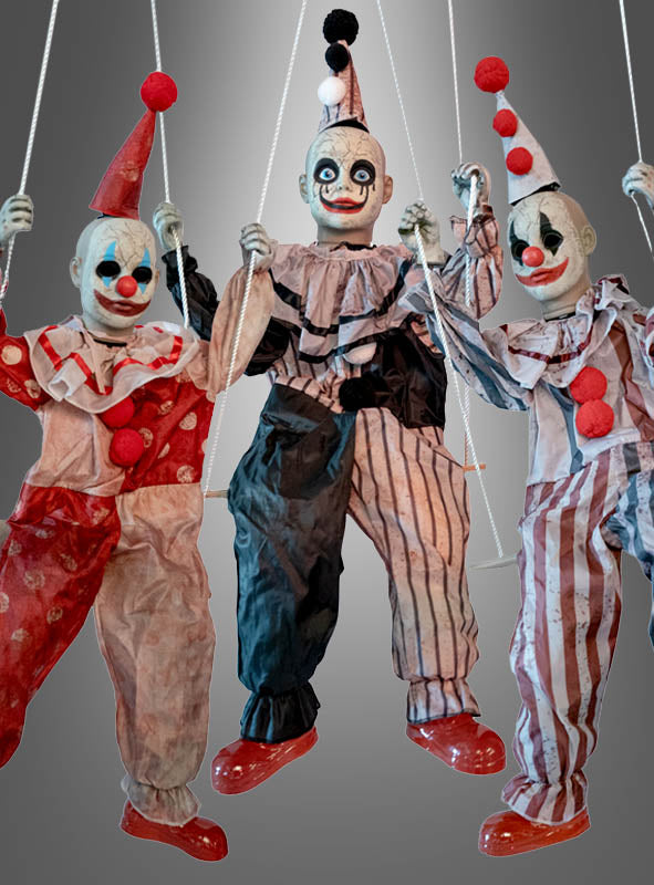 Drei Clown-Puppen in Retro-Kostümen hängen an weißen Schnüren, jede mit bemaltem Gesicht, roter Nase und spitzer Mütze, vor einem grau verlaufenden Hintergrund – das Clown-Trio „Karussell Halloweendeko“ (130 x 220 cm) ist die perfekte Wahl, um bei Ihrer Veranstaltung eine gruselige Atmosphäre zu schaffen.