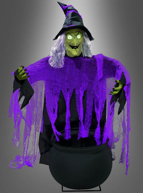 Die sprechende Hexe am Hexenkessel (140 x 96 cm), eine animatronische Figur, trägt einen spitzen Hut, hat leuchtend grüne Augen und zerlumpte lila Kleider und steht hinter einem schwarzen Kessel – die perfekte Halloween-Dekoration für eine gruselige Atmosphäre.