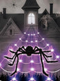 Eine große Spinne mit leuchtend roten Augen sitzt auf dem LED-Spinnennetz (5 Meter mit Spinne) vor einem gruseligen, alten Haus; zusätzliche Spinnen und Spinnennetze schmücken das Gebäude und sorgen so für die perfekte Halloween-Dekoration.