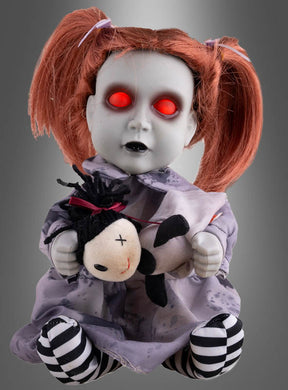 Eine animierte Horrorpuppe (26 cm) mit leuchtenden Augen sitzt vor einem grauen Hintergrund – eine Puppe mit rot leuchtenden Augen, blasser Haut und roten Zöpfen, die ein kleines Stofftier umklammert – perfekt als Halloween-Dekoration, um Ihrem Raum eine unheimliche Note zu verleihen.