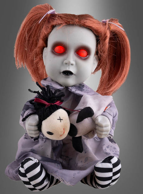 Eine animierte Horrorpuppe (26 cm) mit leuchtenden Augen sitzt vor einem grauen Hintergrund – eine Puppe mit rot leuchtenden Augen, blasser Haut und roten Zöpfen, die ein kleines Stofftier umklammert – perfekt als Halloween-Dekoration, um Ihrem Raum eine unheimliche Note zu verleihen.