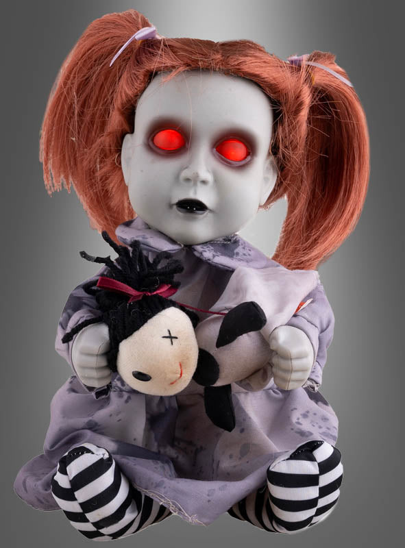 Eine animierte Horrorpuppe (26 cm) mit leuchtenden Augen sitzt vor einem grauen Hintergrund – eine Puppe mit rot leuchtenden Augen, blasser Haut und roten Zöpfen, die ein kleines Stofftier umklammert – perfekt als Halloween-Dekoration, um Ihrem Raum eine unheimliche Note zu verleihen.