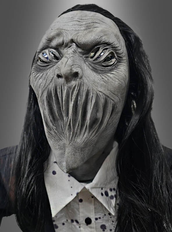 Die Figur trägt eine detailreiche „Gigantischer Zombie 230 cm“-Animatronik-Maske mit verzerrten Gesichtszügen, hohlen Augen und langen vertikalen Schlitzen als Mund und erinnert an einen hoch aufragenden Friedhofsgeist. Mit ihrem langen schwarzen Haar und einem Hemd mit Kragen vermittelt sie den gruseligen Eindruck einer beunruhigenden Halloween-Figur, die zum Leben erweckt wurde.