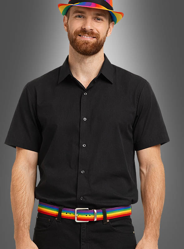 Eine Person in einem schwarzen kurzärmeligen Hemd und einer Hose trägt einen Regenbogengürtel, ein verstellbares Regenbogenarmband und einen Hut und steht vor einem grauen Hintergrund.