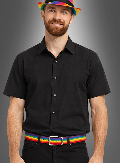 Eine Person in einem schwarzen kurzärmeligen Hemd und einer Hose trägt einen Regenbogengürtel, ein verstellbares Regenbogenarmband und einen Hut und steht vor einem grauen Hintergrund.