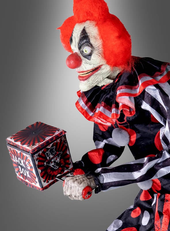 Eine Person in einem furchteinflößenden Halloween-Kostüm namens „Riesige Clownfigur 175 cm, animiert“ mit roten Haaren und gepunkteter Kleidung dreht vor einem grauen Hintergrund die Kurbel einer Springpuppe und sorgt so für eine unheimliche, animierte Halloween-Dekoration.