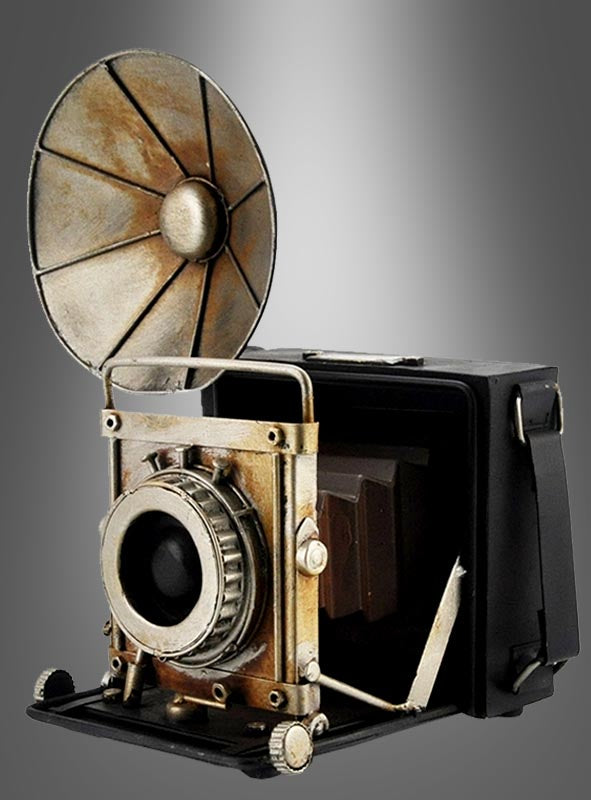 Retro-Fotoapparat mit Blitz – Deko-Kamera mit großem, rundem Blitzreflektor und Metallrädern, die an eine alte Kastenkamera erinnert, präsentiert vor einem grau verlaufenden Hintergrund.