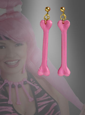 Im Mittelpunkt stehen zwei „Pink Steinzeit Ohrringe Knochen“ – verspielte, knochenförmige Ohrringe in Rosa mit goldenen Haken, die einen verspielten prähistorischen Stil unterstreichen. Im unscharfen Hintergrund trägt eine Frau ein passendes rosa-schwarzes Kostüm. Ideal als ausgefallener Schmuck (Steinzeitfrau-Schmuck) oder als Clip-Ohrringe für Ihre nächste Kostümparty.