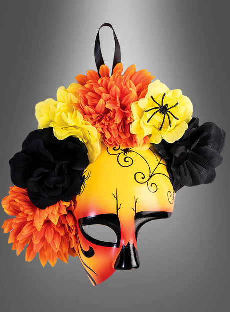 Gelbe und orangefarbene Halloween-Maskenball-Halbmaske, verziert mit großen Kunstblumen, schwarzen Wirbelmustern und einer kleinen schwarzen Spinne, vor einem grauen Hintergrund mit Farbverlauf.