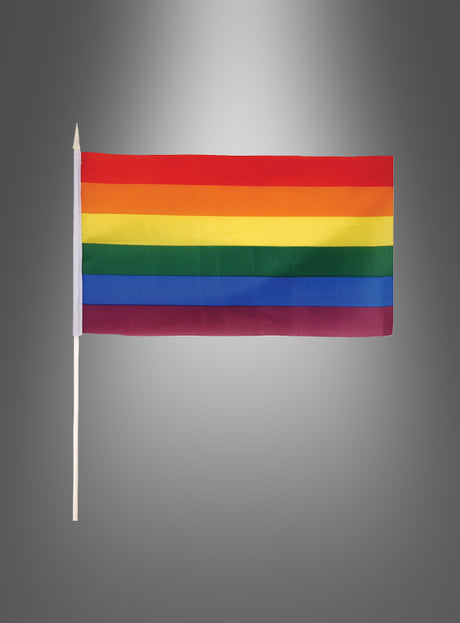 Die Stockfahne „Flagge Regenbogen“ (29 x 17 cm) mit sechs horizontalen Streifen, die an die ikonische Regenbogenfahne erinnern, ist an einem Mast vor einem grauen Hintergrund mit Farbverlauf zu sehen.