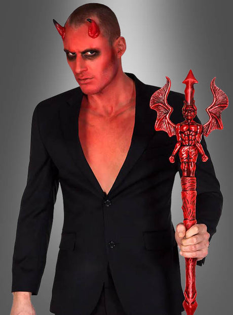 Ein Mann in einem schwarzen Anzug mit roter Haut, roten Teufelshörnern und schwarzem Augen-Make-up hält den „Gothic Stab rot 90 cm Teufel“ in der Hand – einen auffälligen roten Stab –, der sich perfekt als Teufel-Kostüm-Accessoire für Ihre Halloween-Dekoration eignet.
