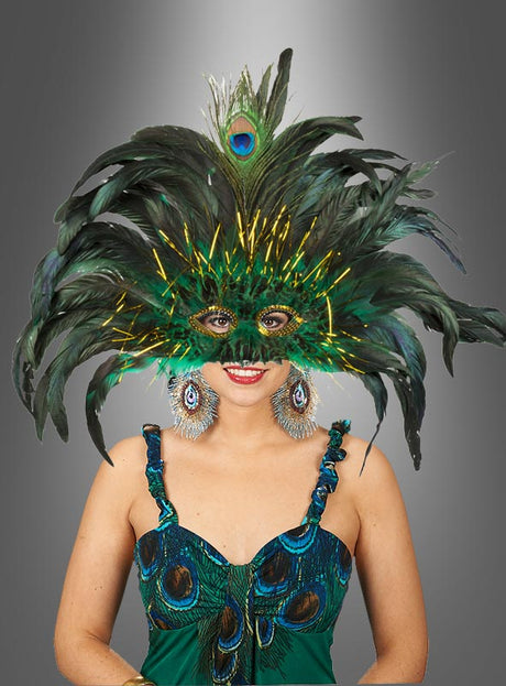 Eine Frau in einem aufwendig gearbeiteten „Samba Federschmuck Pfau“-Kostüm, bestehend aus einer auffälligen, von einem Pfau inspirierten Maske und passenden Ohrringen, steht vor einem grau abgestuften Hintergrund.