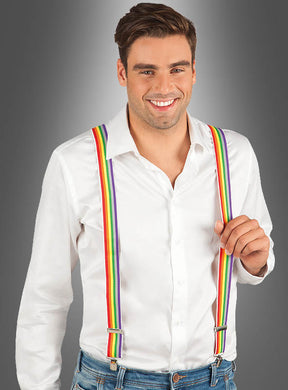 Ein Mann in einem weißen Hemd, blauen Jeans und gestreiften Hosenträgern in Regenbogenfarben – ein perfektes Clown-Accessoire – steht vor einem grauen Hintergrund mit Farbverlauf und lächelt in die Kamera.