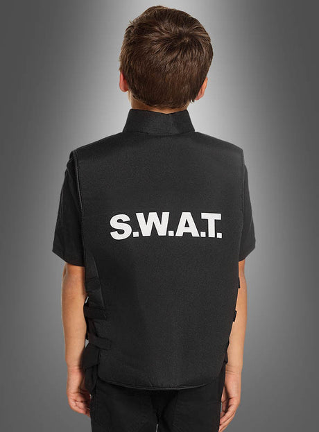 Ein Kind, das mit dem Rücken zur Kamera steht, trägt eine schwarze SWAT-Weste für Kinder, auf deren Rücken in weißen Buchstaben vor grauem Hintergrund „S.W.A.T.“ steht.